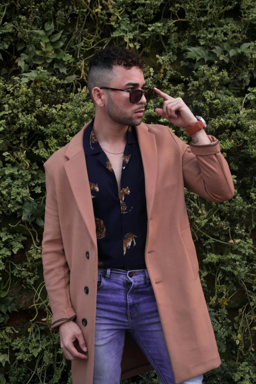 a man standing in front of bushes talking on a cell phone, an album cover, trending on pexels, renaissance, wearing a purple detailed coat, wearing orange sunglasses, light brown trenchcoat, young spanish man