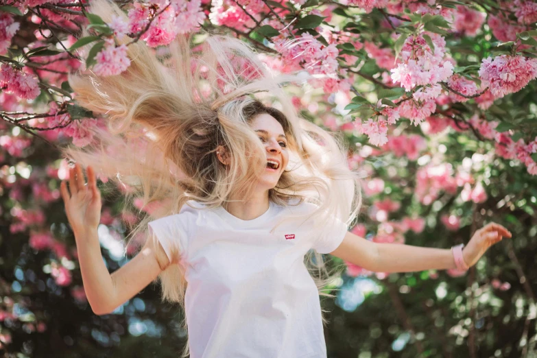 a woman with her hair blowing in the wind, pexels contest winner, cherry blosom trees, wearing a t-shirt, happy friend, white and pink