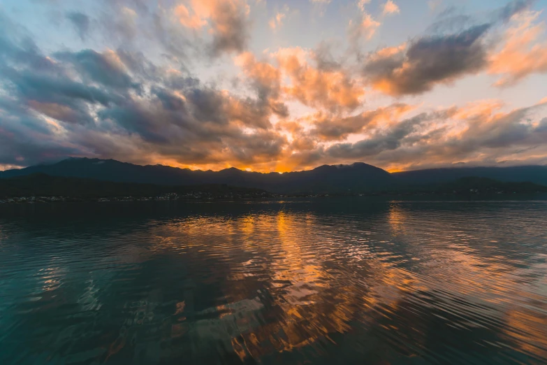 a sunset over a body of water with mountains in the background, by Niko Henrichon, pexels contest winner, clouds around, boka, multiple stories, soft light 4k