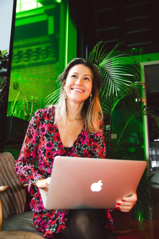 a woman sitting on a couch with a laptop, a portrait, by Julia Pishtar, happening, next to a plant, background bar, smiling, very vibrant