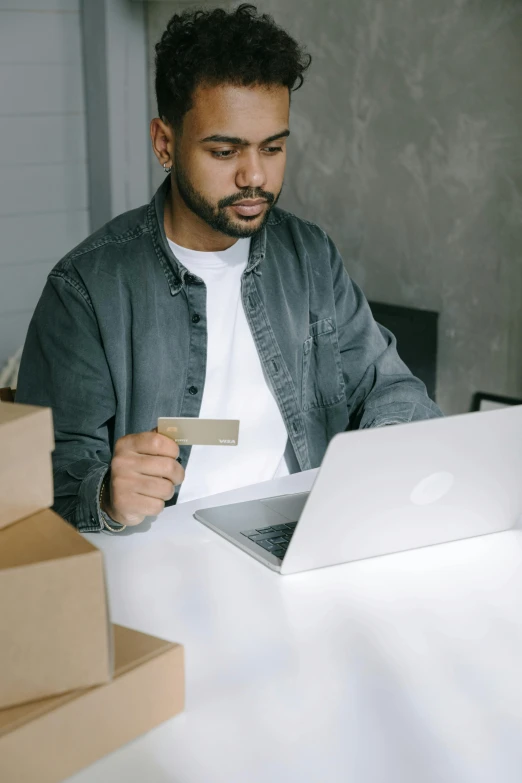 a man sitting at a table with a laptop and a credit card, delivering packages for amazon, slightly minimal, riyahd cassiem, thumbnail