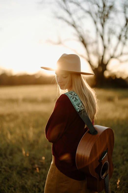 a woman standing in a field holding a guitar, golden hour photograph, profile pic, straps, backlighted