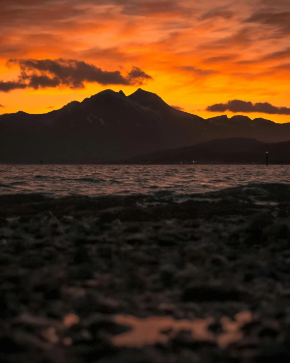 a sunset over a body of water with mountains in the background, by Robbie Trevino, unsplash contest winner, mount doom, shoreline, brown, skye meaker