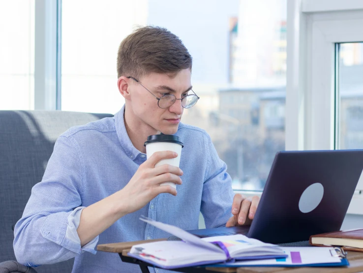 a man sitting at a table with a laptop and a cup of coffee, academic art, lachlan bailey, school curriculum expert, profile image, non-binary