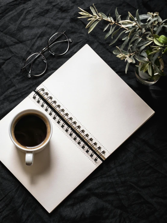 a cup of coffee and a notebook on a bed, trending on unsplash, minimalism, on black paper, wearing black rimmed glasses, high-quality photo, no - text no - logo