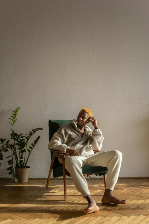 a man sitting in a chair in a room, an album cover, inspired by Barthélemy Menn, trending on pexels, white pants, morning mood, green corduroy pants, african man