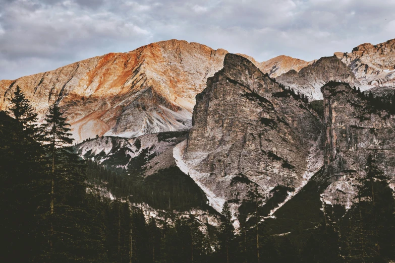 a mountain range with trees and mountains in the background, a photo, unsplash contest winner, baroque, gray and orange colours, chiseled features, multiple stories, early evening