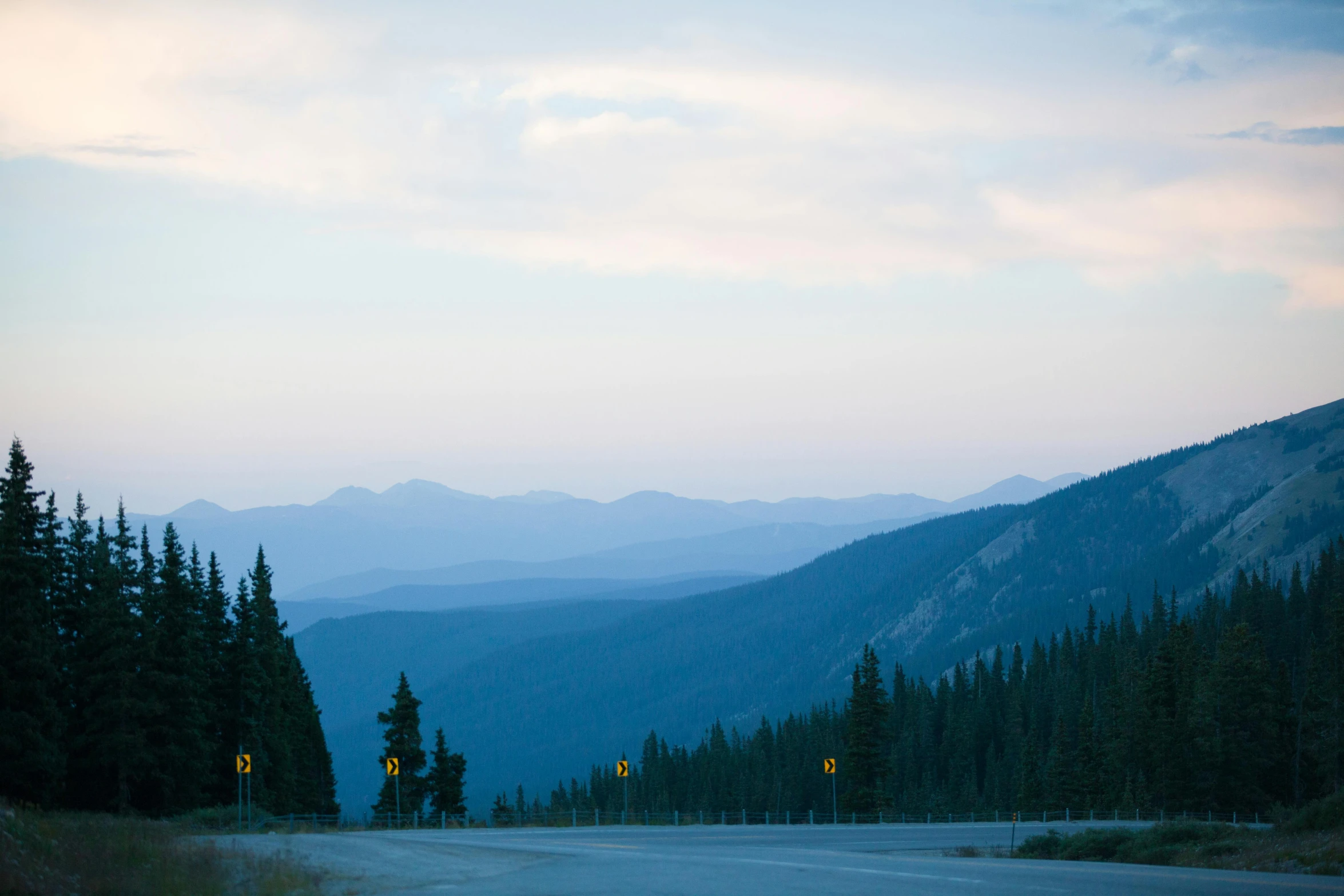 a couple of signs on the side of a road, by Emma Lampert Cooper, trending on unsplash, colorado mountains, calm evening, whistler, seen from far away