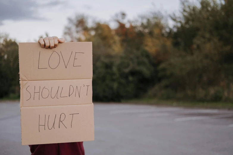 a person holding a sign that says love shouldn't hurt, trending on pexels, hurufiyya, injured, thumbnail, exterior shot, plain