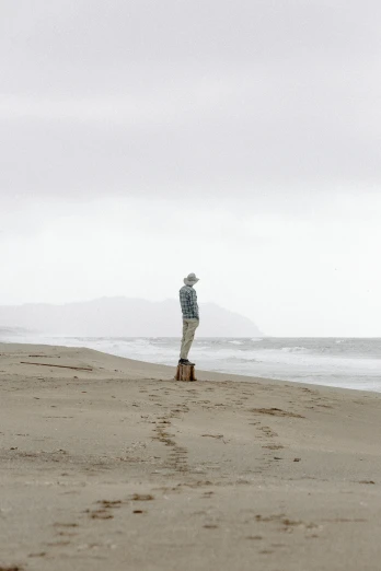 a man standing on top of a sandy beach next to the ocean, a picture, by Eglon van der Neer, unsplash, conceptual art, alec soth : : love, gray men, california, waiting