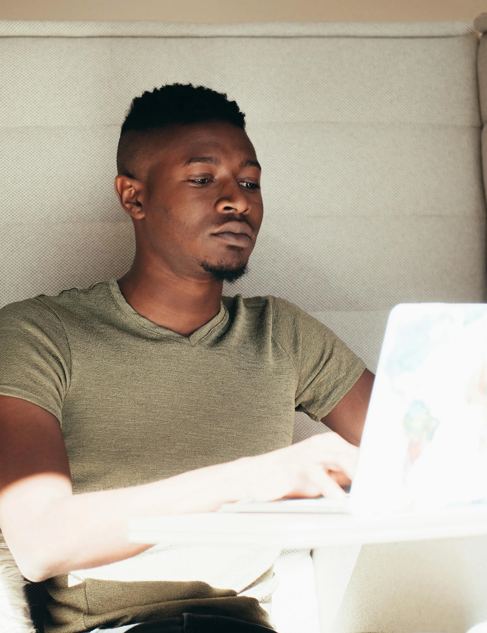 a man sitting on a couch using a laptop computer, a screenshot, by Carey Morris, trending on unsplash, man is with black skin, trans rights, in a dark green polo shirt, non binary model