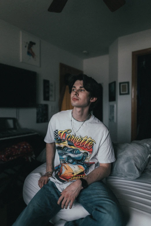 a man sitting on top of a bed in a bedroom, an album cover, by Robbie Trevino, trending on pexels, wearing a t-shirt, he is about 2 0 years old, slightly smirking, jay bauman