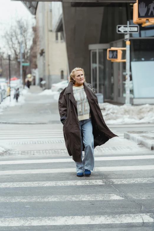 a woman walking across a crosswalk in the snow, inspired by Louisa Matthíasdóttir, happening, light brown trenchcoat, non-binary, humans of new york, gillian anderson