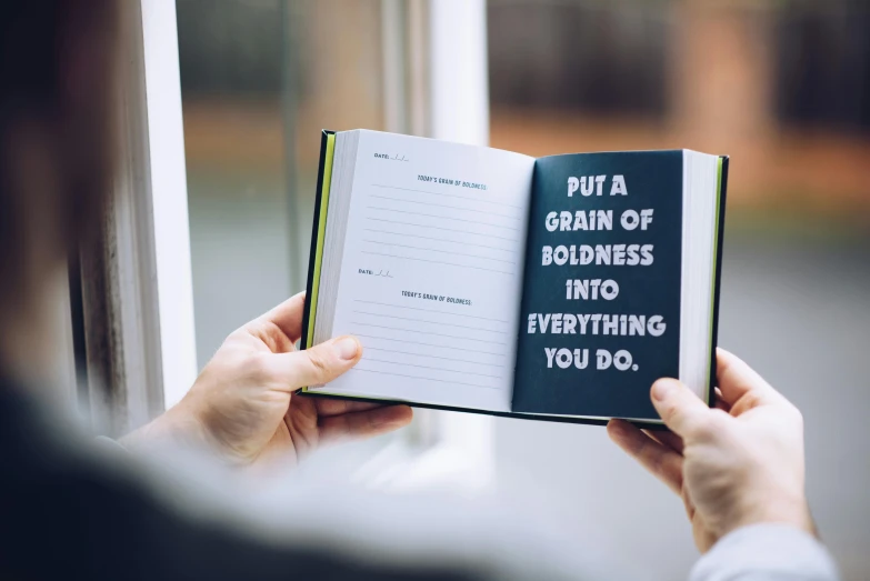 a person holding a book that says put a grain of goodness into everything you do, by Julia Pishtar, letterism, wide shot photograph, karl pilkington, slash page, fully functional