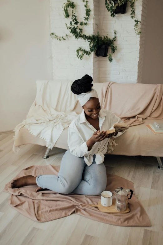 a woman sitting on the floor reading a book, by Dulah Marie Evans, having a snack, goddess checking her phone, wearing a white button up shirt, light beige pillows