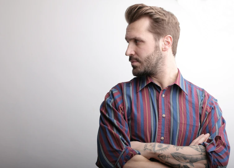 a man with a tattoo on his arm, inspired by Alexander Scott, pexels, bauhaus, wearing stripe shirt, brown red blue, beard stubble, looking off into the distance