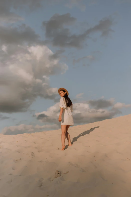 a woman standing on top of a sandy hill, trending on pexels, nico wearing a white dress, partly cloudy, with hat, sha xi