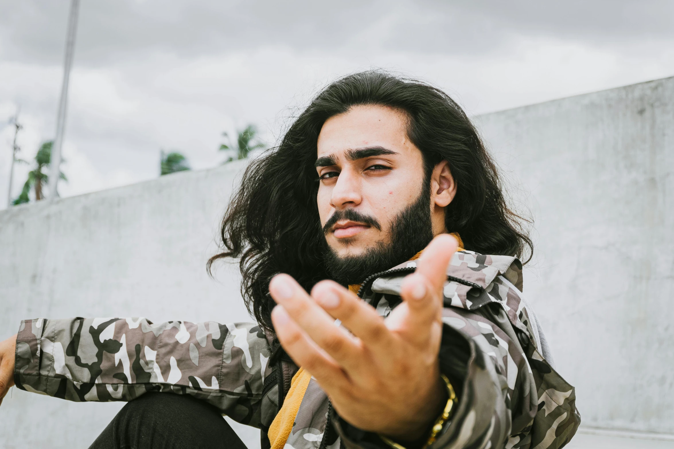 a man with long hair sitting on a skateboard, trending on pexels, visual art, middle eastern skin, pointing at the camera, headshot profile picture, militaristic