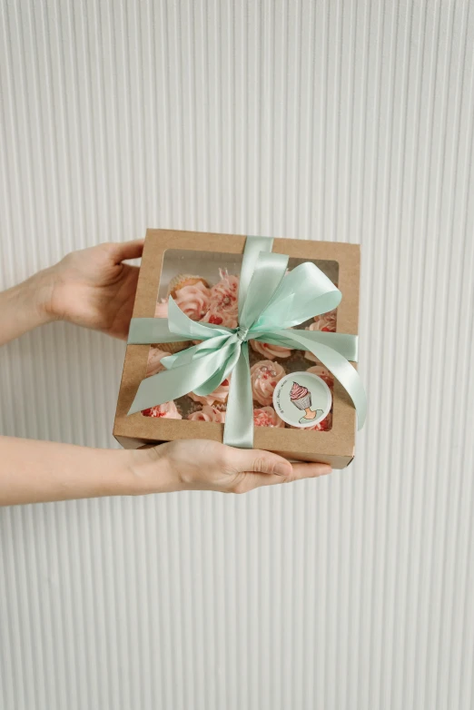 a person holding a box with cupcakes in it, jakarta, ribbon, tan, small