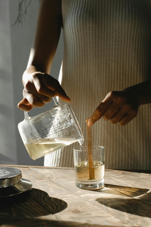 a person pouring something into a glass on a table, curated collections, square, vanilla, medium