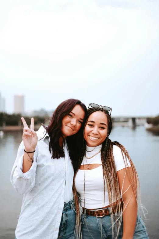 two women standing next to each other near a body of water, peace sign, college party, profile image, trending on tiktok