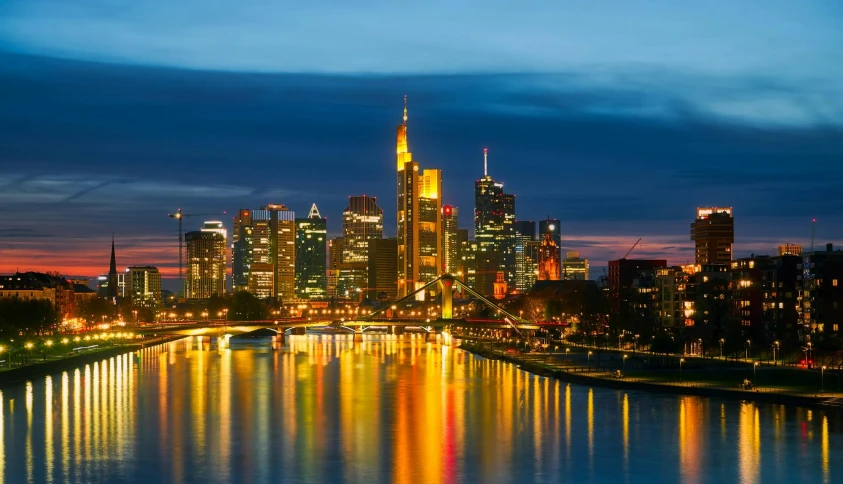 a large body of water with a city in the background, by Niko Henrichon, pexels contest winner, the river is full of lights, gold glow, germany. wide shot, conde nast traveler photo