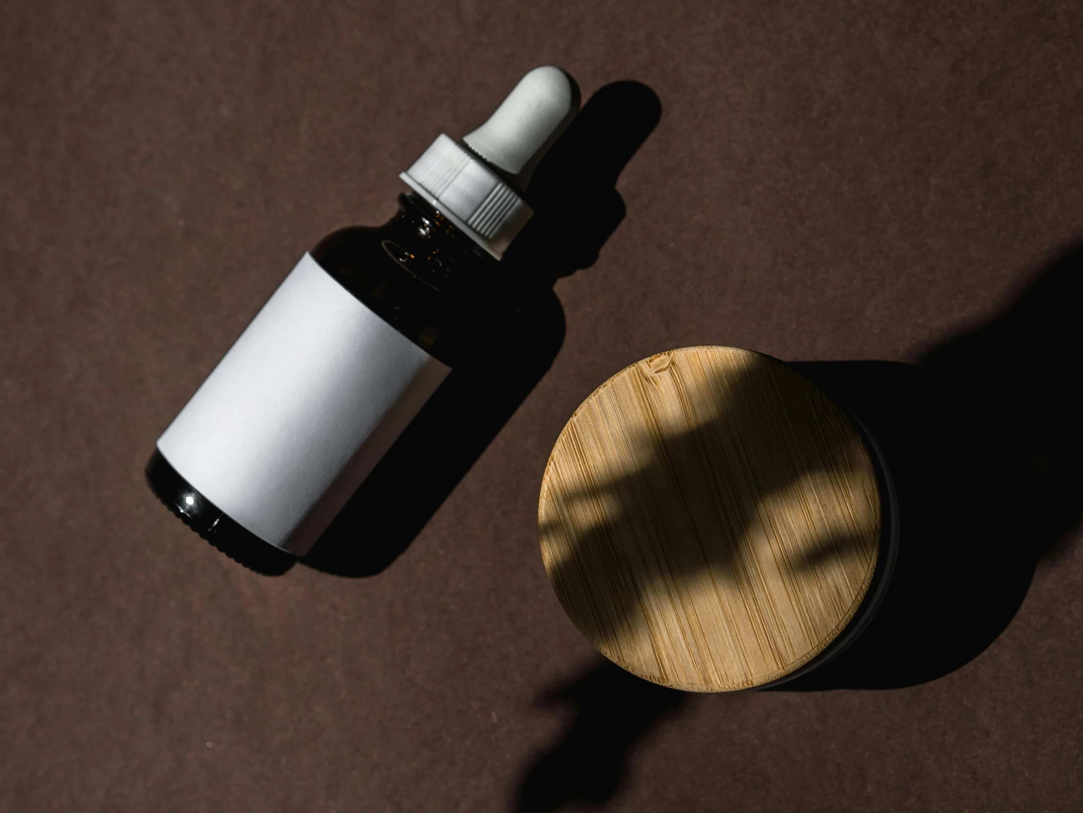 a bottle of essential oil next to a wooden container, trending on pexels, minimalism, dark and white, round format, organic shape, lacquered