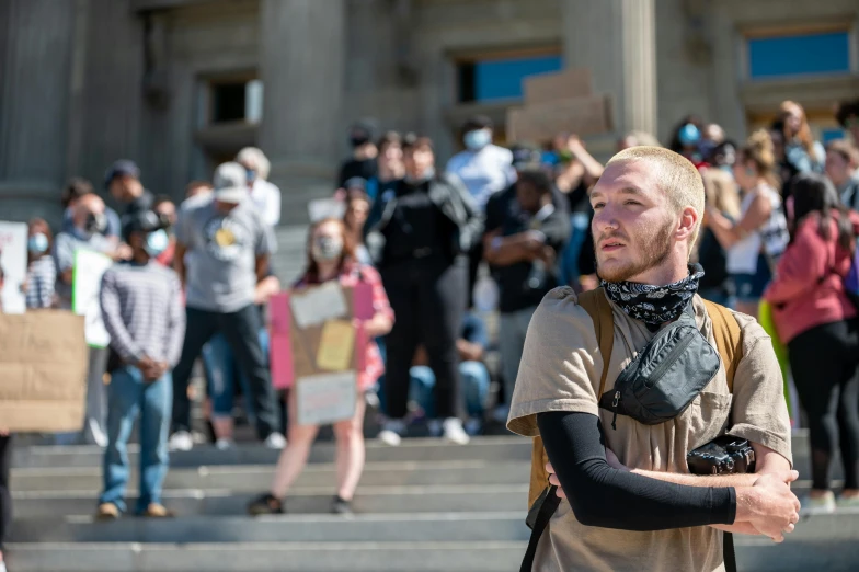 a man standing in front of a crowd of people, a photo, by Dan Frazier, trending on reddit, protest, a man wearing a backpack, deteriorated, zach hill