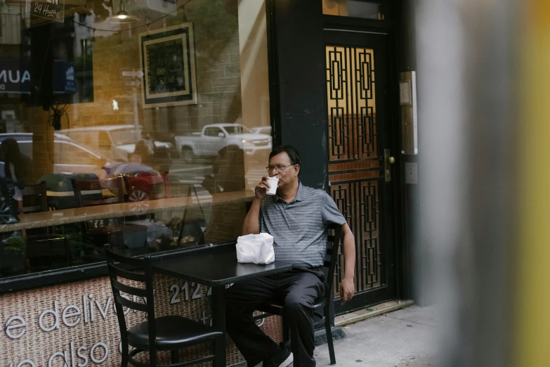 a man sitting at a table talking on a cell phone, by William Berra, unsplash, realism, location [ chicago ( alley ) ], iced latte, ethiopian, 2000s photo