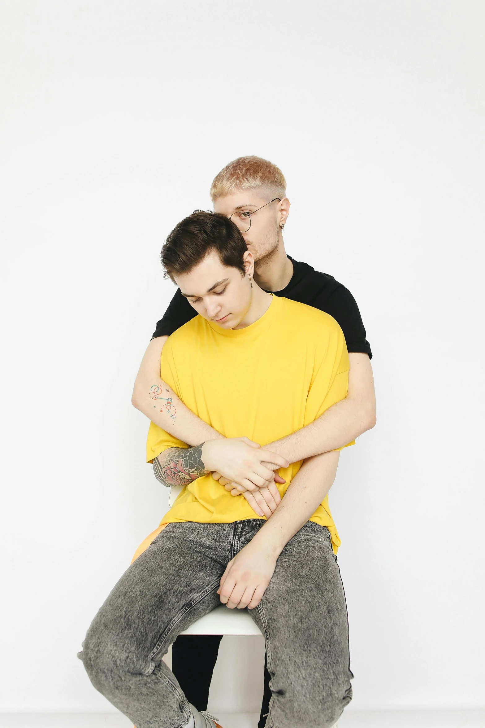 a man and a woman sitting on a stool, an album cover, unsplash, wearing a modern yellow tshirt, two men hugging, very very very pale skin, catalog photo