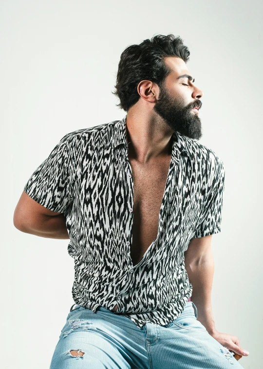 a man with a beard sitting on a stool, an album cover, inspired by Germán Londoño, trending on unsplash, patterned clothing, back and white, indian super model, dirty short sleeved shirt