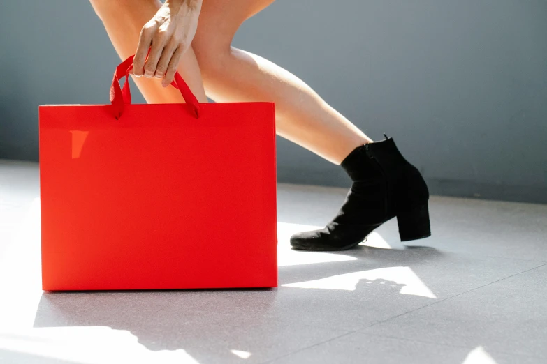 a woman is holding a red shopping bag, by Julia Pishtar, pexels contest winner, minimalism, sleek legs, matte accents, sitting on a store shelf, stunning design