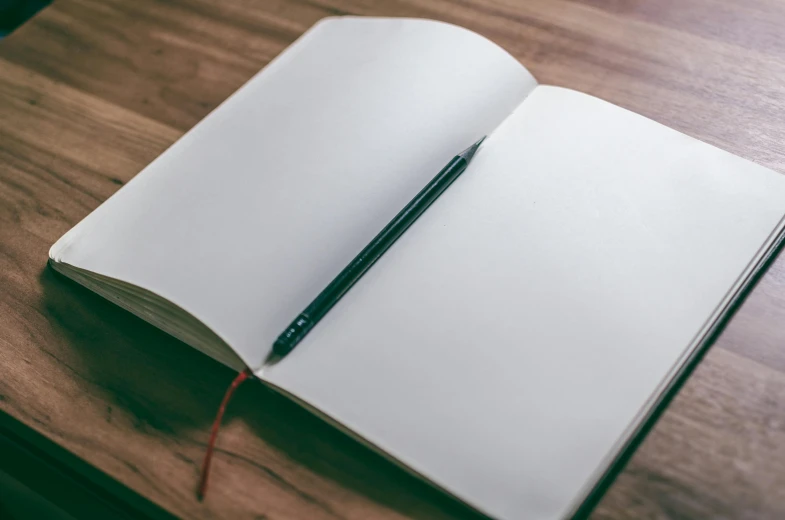 an open notebook sitting on top of a wooden table, a drawing, unsplash, black ball pen on white paper, background image, big open book, rectangular