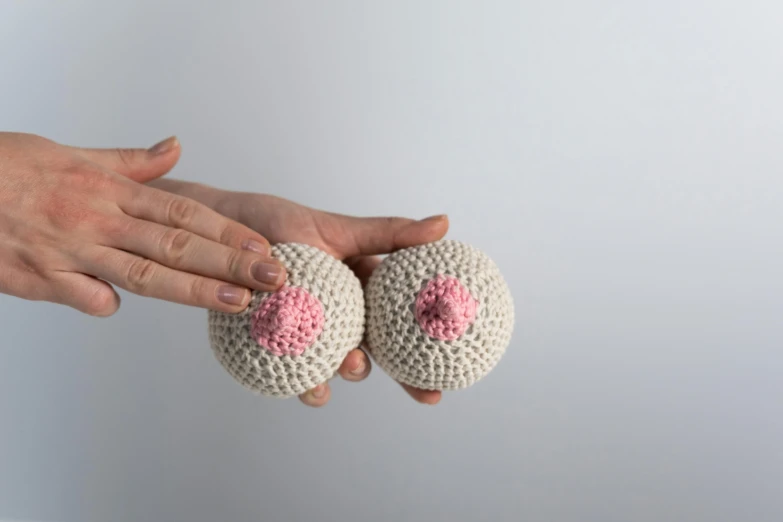 a person holding two crocheted doughnuts in their hands, inspired by Louise Bourgeois, unsplash, large breasts size, prosthetic eyeballs, white and pink, crochet skin