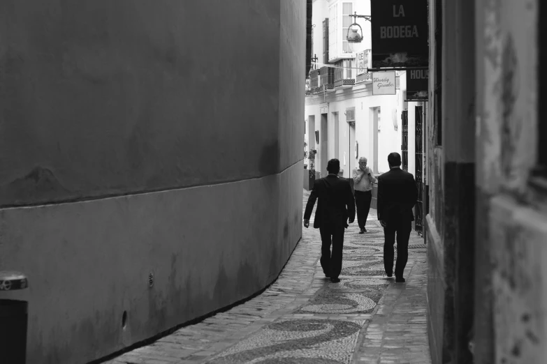 a couple of people that are walking down a street, a black and white photo, by Altichiero, business men, jerez, three, dingy city street