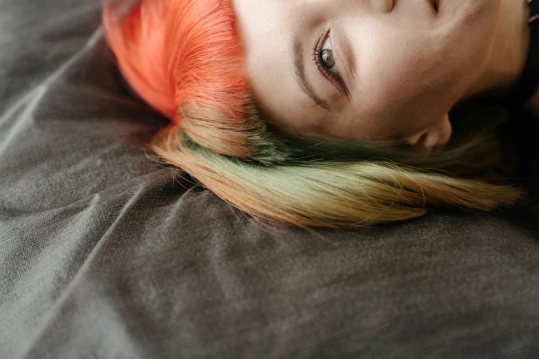 a close up of a person laying on a bed, inspired by Elsa Bleda, trending on pexels, renaissance, multicolored hair, orange head, green and black hair, colorful]”