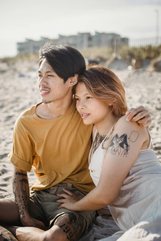 a man and woman sitting next to each other on a beach, a tattoo, trending on pexels, asian descent, androgynous person, looking her shoulder, headshot