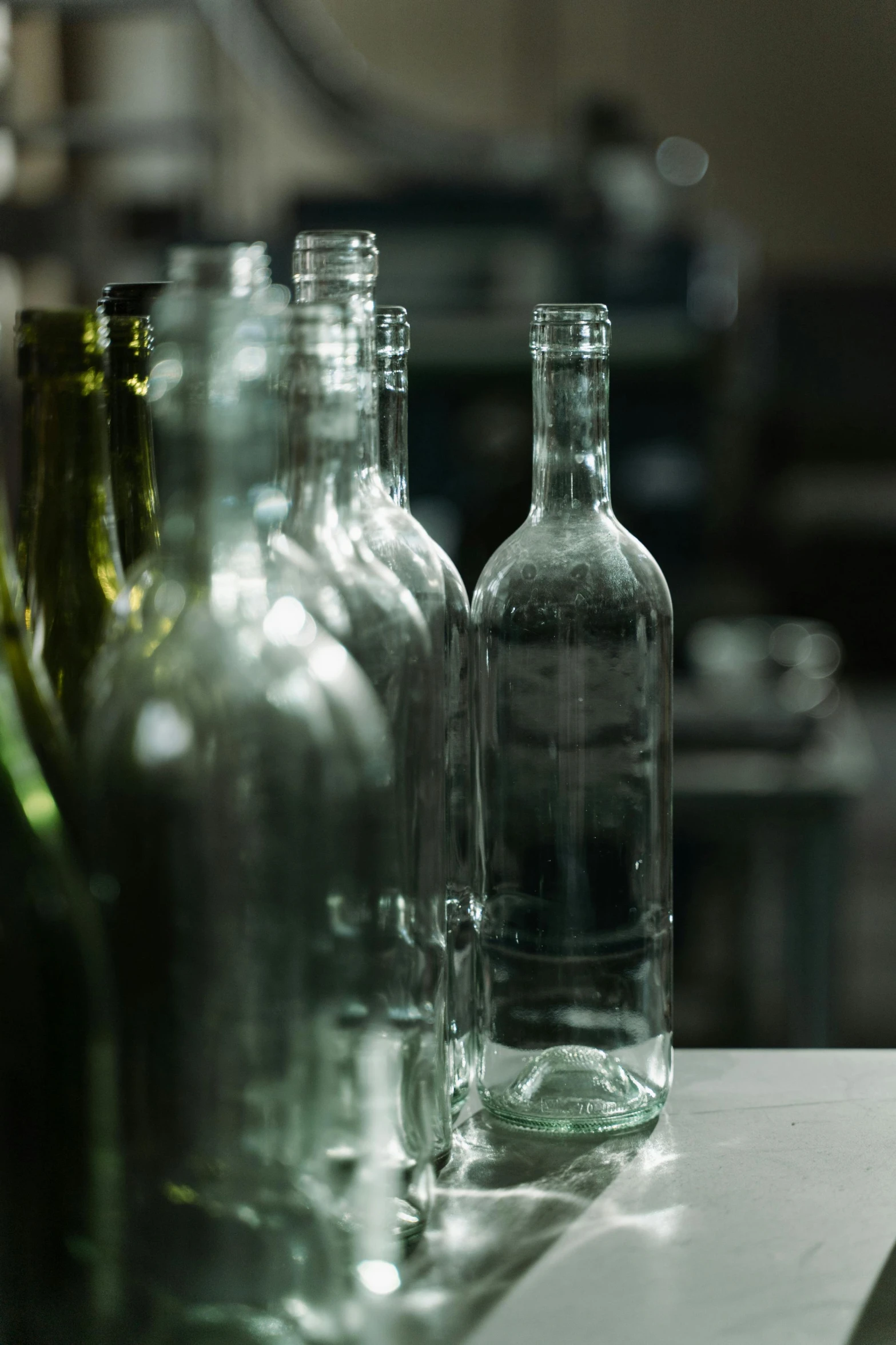 a row of empty bottles sitting on top of a counter, a still life, unsplash, multiple stories, back room, grey, made out of glass