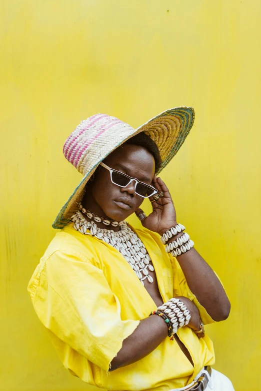 a woman standing in front of a yellow wall talking on a cell phone, an album cover, trending on pexels, afrofuturism, covered in jewels, lupita nyong'o, wearing wide sunhat, shades of yellow