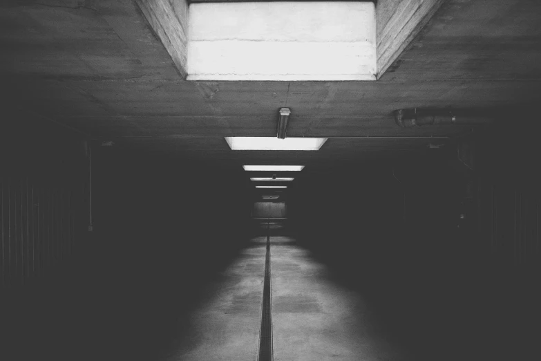 a black and white photo of a long hallway, unsplash, light and space, lighting on concrete, scary lighting, ceiling fluorescent lighting, concrete