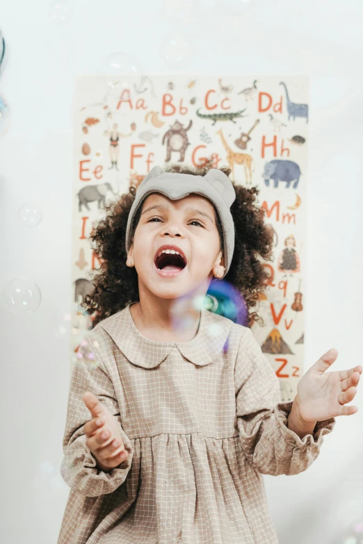 a little girl standing in front of a christmas tree, pexels contest winner, art & language, bubbles in the air, wearing a grey wizard hat, earing a shirt laughing, nursery poster