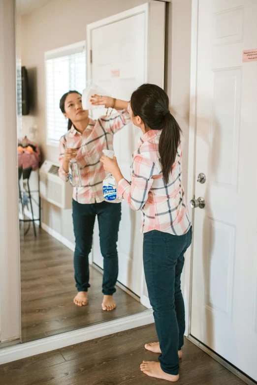 a woman standing in front of a mirror brushing her teeth, by Nicolette Macnamara, pexels contest winner, jeans and t shirt, asian descent, spraying liquid, low quality photo