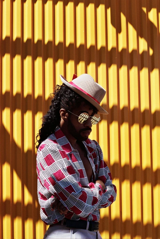 a man standing in front of a yellow wall, by Carey Morris, trending on pexels, op art, long afro hair, wearing a fedora, al fresco, checkered spiked hair