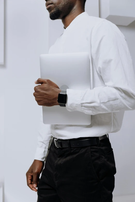 a man in a white shirt and black pants holding a laptop, by Carey Morris, office clothes, close - up photograph, multiple stories, dark-skinned
