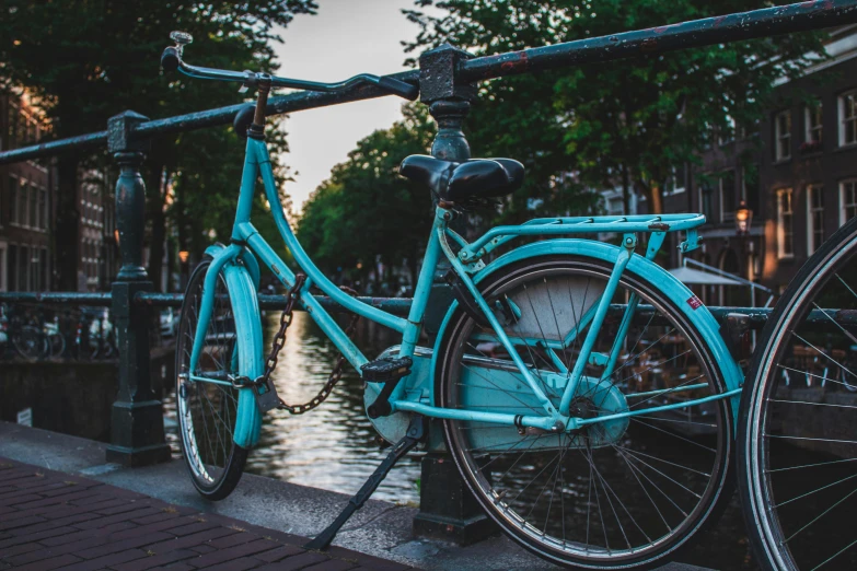 a blue bicycle parked on a bridge next to a body of water, by Jan Tengnagel, pexels contest winner, brown and cyan color scheme, avatar image, amsterdam, in the evening