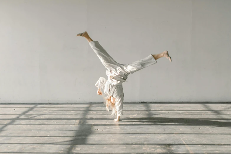 a person doing a handstand in a room, arabesque, wearing white suit, wearing human air force jumpsuit, triumphant pose, white concrete floor