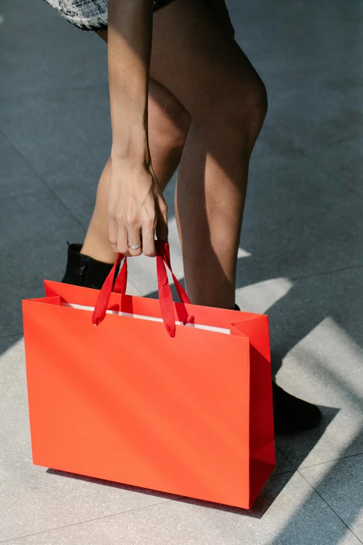 a woman is holding a red shopping bag, by Julia Pishtar, pexels contest winner, wearing red shorts, sephora, detail shot, sustainability