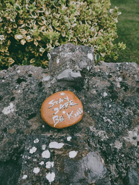 a stone with writing on it sitting on a rock, an album cover, by Sophia Beale, unsplash, kindness, badge, okay, tan