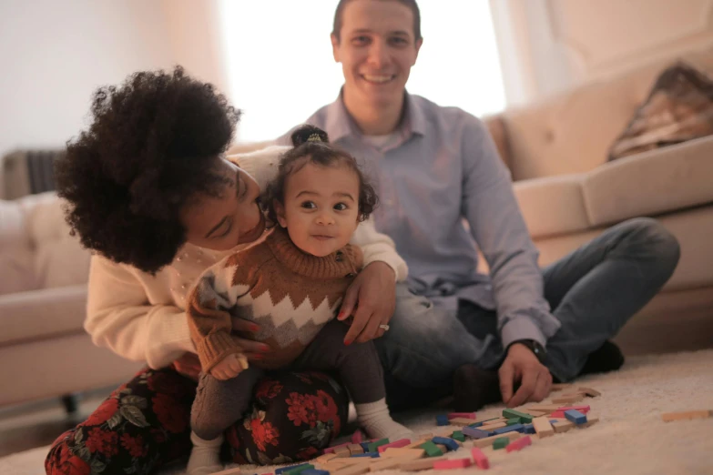 a woman sitting on the floor playing with a child, by Tom Carapic, pexels contest winner, portrait of family of three, mixed race, avatar image, father with child