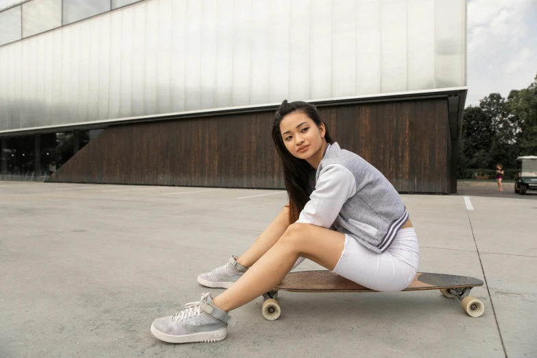 a woman sitting on a skateboard in front of a building, white and grey, dilraba dilmurat, confident relaxed pose, sport clothing